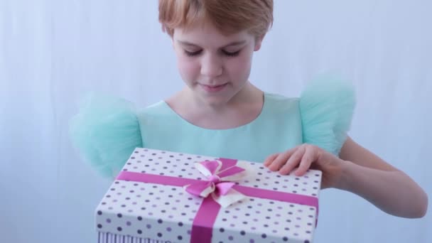En teenagepige i en smuk aftenkjole. Barnet åbner kassen med gaven. Følelserne af overraskelse og lykke fra overraskelsen i kassen – Stock-video