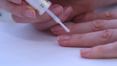 Kadınların elleri kapalı olsun. Kız tırnaklarını şeffaf bir tıbbi cilayla kaplıyor. Doğal manikür. Tırnak bakımı. Terapi maddelerinin yardımıyla tırnaklarımı güçlendiriyorum.