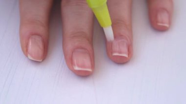Kadınların elleri kapalı olsun. Kız tırnaklarını özel bir tırnak altı yağıyla kaplıyor. Tırnak bakımı. Cilt yumuşaması, kütikül büyümesi önleme