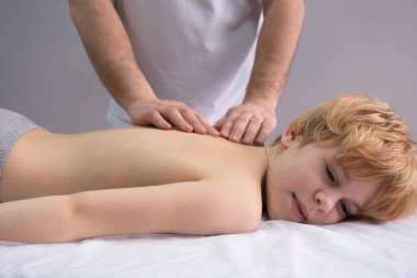Osteopat omurgayla çalışıyor. Genç bir çocuk bir doktorun önündeki kanepede yatıyor. Bir kayropraktik uzmanı omurgayı inceler. Duruş düzeltmesi