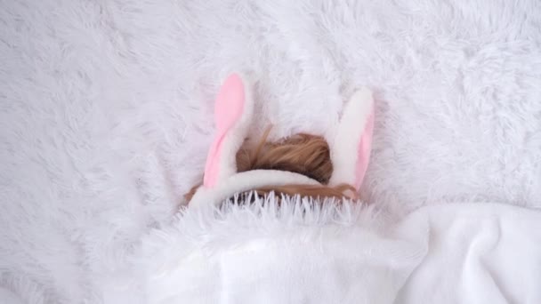 Rabbit ears are visible from under a fluffy white plaid. Easter waiting concept. Ears rise and fall as the child plays. Festive mood, joke. Soft pastel shades. Waiting for Easter — Stock Video