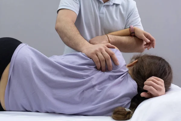 Un chiropraticien palpe la zone de l'omoplate sur le dos du patient. Rendez-vous avec un ostéopathe. La fille est allongée sur le canapé, le docteur travaille avec son dos. Vue arrière — Photo