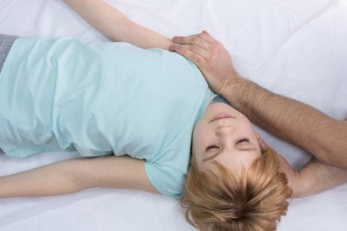 Doktor servikal omurga üzerinde çalışıyor. Osteopat hastaların boynunu gerer. Genç bir çocuk kanepede doktorun önünde yatıyor. Doktor boynun hareketini belirler.