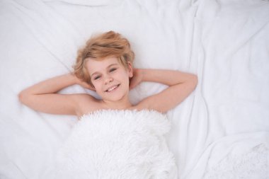 Güzel bir genç kız yatakta yatıyor. Mutlu çocuk gülümsemesi. İyi uyku ve keyifli uyanış kavramı. Beyaz pofuduk battaniye. Metin için yer var. Samimi duygular