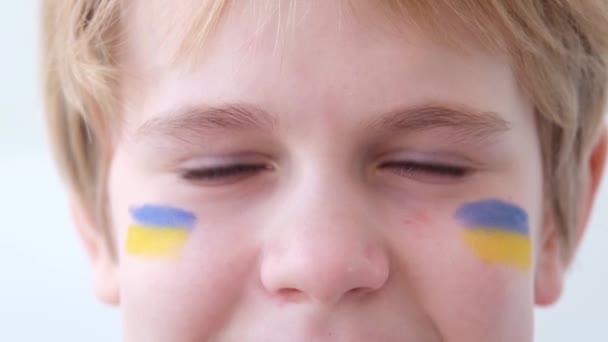 Gözlerin yaşla dolu. Çocukça gözlere yakın çekim. Yüzünde Ukrayna bayrağı olan bir çocuk. Savaş konsepti. Ukrayna, 2022 — Stok video