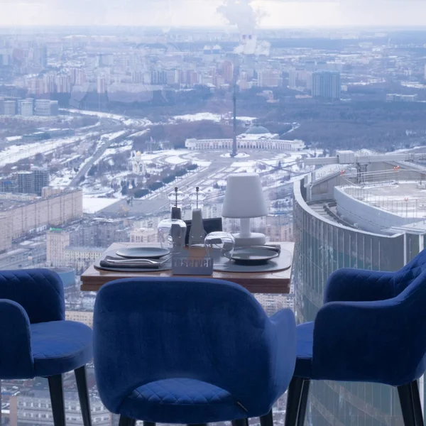 Splendida vista della città dalla finestra del ristorante. In primo piano un tavolo con posate e poltrone accoglienti. Fuori dalla finestra c'è un panorama della città invernale — Foto Stock