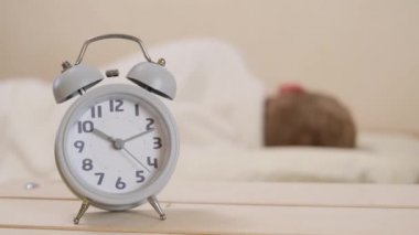 Gri alarm saati ahşap bir masanın üzerinde duruyor. Arka planda uyuyan bir adamla bir yatak var. Sabah konsepti, uyanış. Kopyalama alanı.