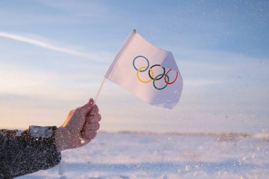 Eldeki küçük Olimpiyat bayrağı kar ve ağaçların zemininde dalgalanıyor. 2022 Kış Olimpiyat Oyunları kavramı..