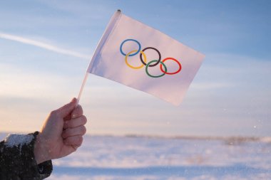 Eldeki küçük Olimpiyat bayrağı kar ve ağaçların zemininde dalgalanıyor. 2022 Kış Olimpiyat Oyunları kavramı..