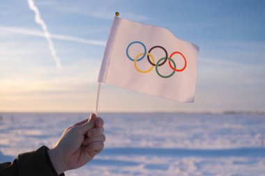 Eldeki küçük Olimpiyat bayrağı kar ve ağaçların zemininde dalgalanıyor. 2022 Kış Olimpiyat Oyunları kavramı..
