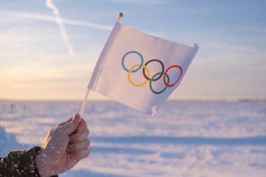 Eldeki küçük Olimpiyat bayrağı kar ve ağaçların zemininde dalgalanıyor. 2022 Kış Olimpiyat Oyunları kavramı..