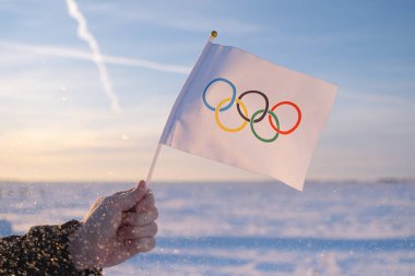 Eldeki küçük Olimpiyat bayrağı kar ve ağaçların zemininde dalgalanıyor. 2022 Kış Olimpiyat Oyunları kavramı..