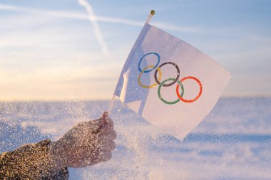 Eldeki küçük Olimpiyat bayrağı kar ve ağaçların zemininde dalgalanıyor. 2022 Kış Olimpiyat Oyunları kavramı..