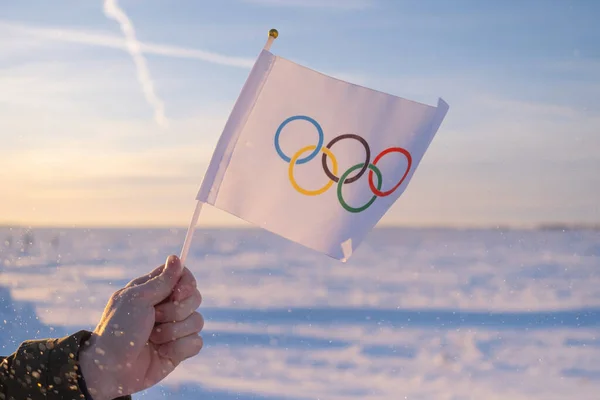 Eldeki küçük Olimpiyat bayrağı kar ve ağaçların zemininde dalgalanıyor. 2022 Kış Olimpiyat Oyunları kavramı..