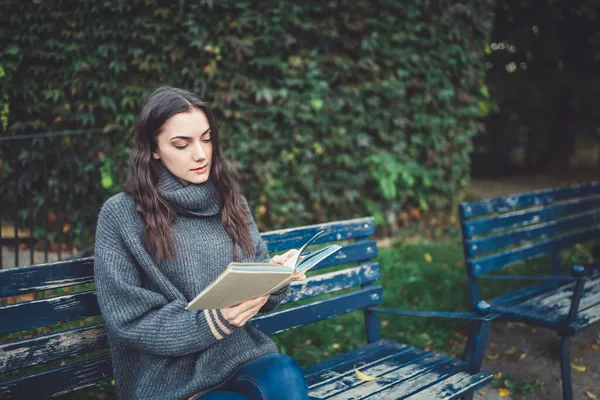 Žena, která čte knihu na lavici v parku — Stock fotografie
