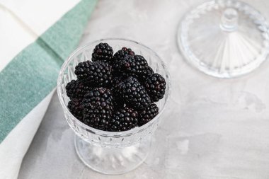 Gri arka planda desenli cam kasede taze böğürtlen