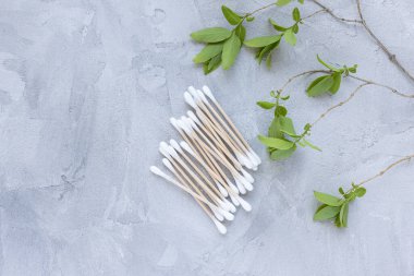 Gri arka planda çevre dostu bambu tomurcukları, yeşil yapraklar. Pamuklu çubuklar, kulak temizleyici çubukları..