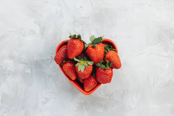 Vers geplukte aardbeien in hartvormige kom op rustieke grijze achtergrond — Stockfoto