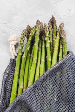 Çevre dostu yeniden kullanılabilir gri arka planda taze çiğ yeşil kuşkonmaz mızrakları. Sağlıklı sebzeler, vejetaryen yemekleri ve yemek pişirme konsepti için malzemeler. Yakın plan, kopyalama alanı.