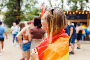 Parktaki sokakta LGBTQI gururlu gökkuşağı bayrağıyla örtünen mutlu sarışın kadın. LGBT Onur Ayı, gurur etkinliği ve Gay geçit töreni konsepti