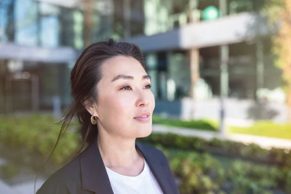 Asian confident business woman in suit smiling, looking up to the bright future of her career opportunities. Job, work aspirational banner, spring background of office center with trees. Business