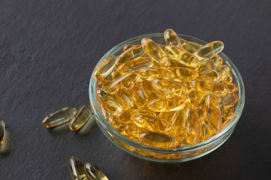 Siyah tahta kaplama arka planda cam kasede balık yağı kapsülleri. Omega 3, E vitamini takviyeleri. Sağlıklı beslenme konsepti. Yakın plan, kopyalama alanı