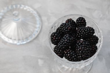Taze böğürtlenler gri arka plandaki cam kasede servis edilir. Sağlıklı vejetaryen yemeği kavramı. Yakın çekim, üst görünüm, seçici odak