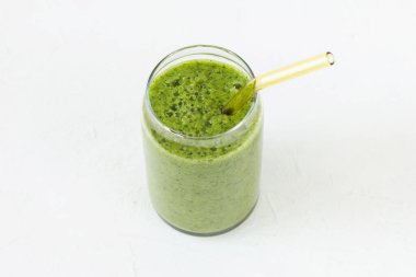 Green smoothie in glass with environmentally friendly drinking glass tube. White background. Vegan, raw, clean, healthy food