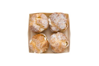 Choux Bun with whipped cream and sugar powder on top in pastry box isolated on white background. Delicate choux pastry dessert. French cream puff. Top view, copy space
