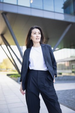Asian confident business woman in suit smiling, looking up to bright future of her career opportunities. Job, work aspirational banner, spring background of office center. Business people lifestyle