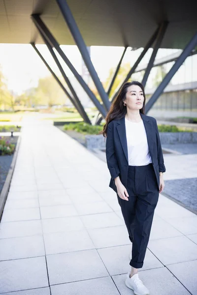 Full body portrait of Asian confident business woman in suit, walking in business center spring, summer or fall park. Job career, office work, business people lifestyle concept