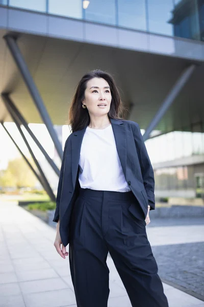 Asian confident business woman in suit smiling, looking up to bright future of her career opportunities. Job, work aspirational banner, spring background of office center. Business people lifestyle