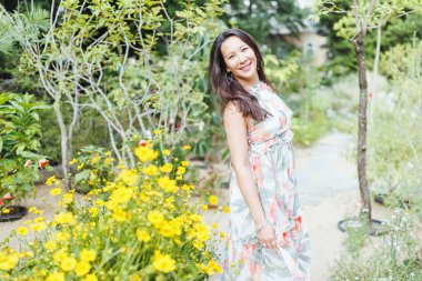 Güzel mutlu melez Japon kadın, yaz parkında romantik bir çiçek desenli elbise giymiş, gülümsüyor. Tam vücut vuruşu. Güneş ışığı, boşluğu kopyala