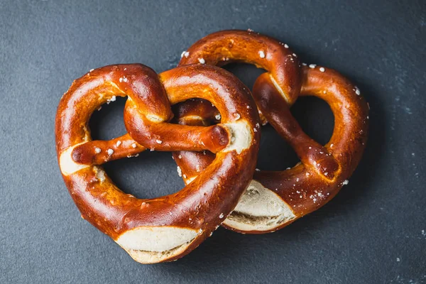 stock image Two homemade freshly baked soft pretzels on black backround. Traditional Bavarian pretzel for Octoberfest. Top view, copy space