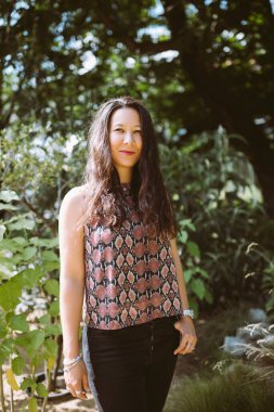 Yaz parkında kot pantolon ve gömlek giymiş güzel, mutlu, melez bir Japon kadın, gülümsüyor.