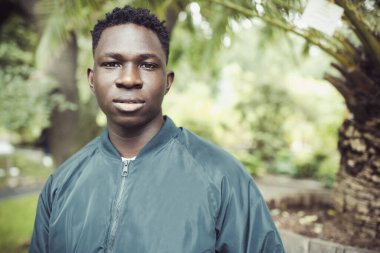 Bombacı ceketli genç Afrikalı bir adam parkta ya da açık havada. Sonbahar ya da bahar mevsimi