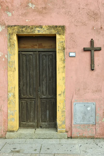 Old wooden doorway with cross on exterior pink wall in Villasimi — Stock Photo, Image