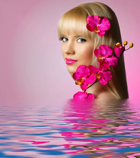 Mulher bonita com flores de orquídea na água — Fotografia de Stock