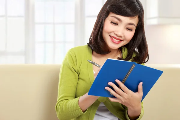 Frau schreibt Buch, während sie auf der Couch sitzt — Stockfoto