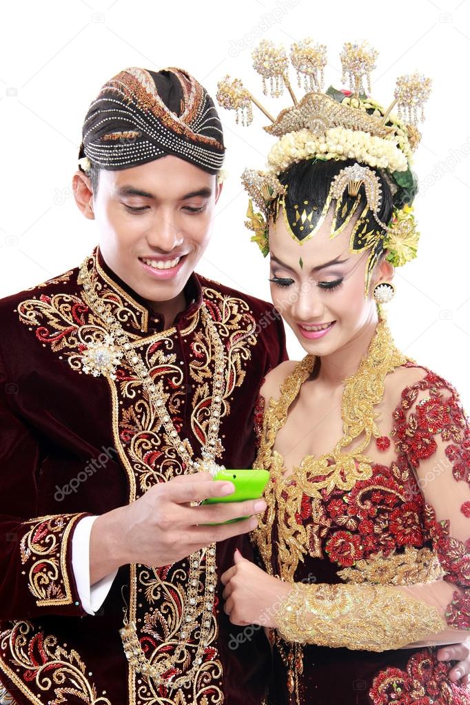 happy traditional java wedding couple with mobile phone