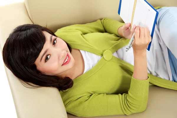 Mujer joven sonriente acostada en un sofá y escribiendo —  Fotos de Stock