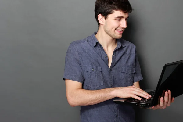 Fiatal férfi mosolyogva, laptop számítógép segítségével — Stock Fotó