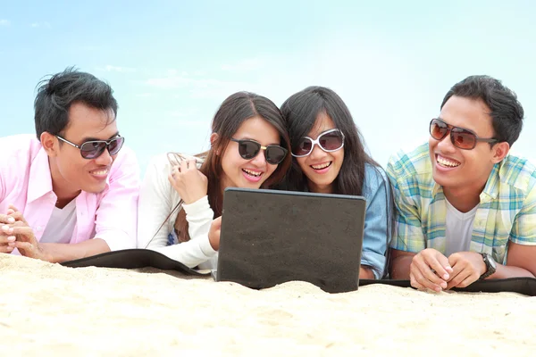Групповые друзья наслаждаются отдыхом на пляже вместе с ноутбуком — стоковое фото