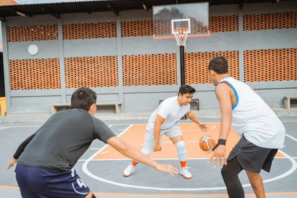 a male basketball player in a white tracksuit dribbles the ball in the face of two opposing players