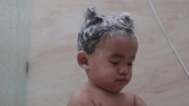 Asyalı çocuk banyoda duş alıyor, saçlarını yıkıyor.