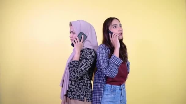 Dos mujeres asiáticas haciendo llamadas telefónicas mientras de pie espalda con espalda — Vídeos de Stock