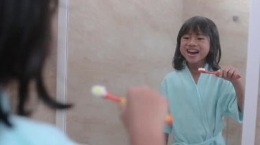 Banyoda dişlerini fırçalayan kız aynaya bakıyor.