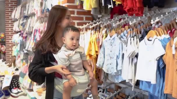 Madre indonesia comprando ropa para su hijo en la tienda boutique de bebés — Vídeos de Stock