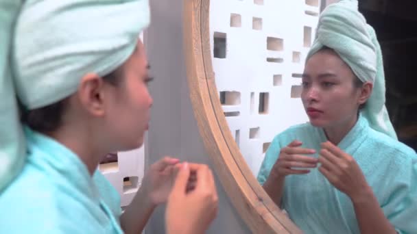 Красивая девушка сжимает прыщ на щеке к зеркалу — стоковое видео