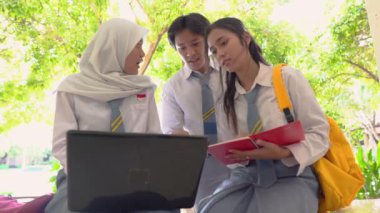 Bir grup lise öğrencisi dizüstü bilgisayar kullanıyor ve kitap taşıyor.